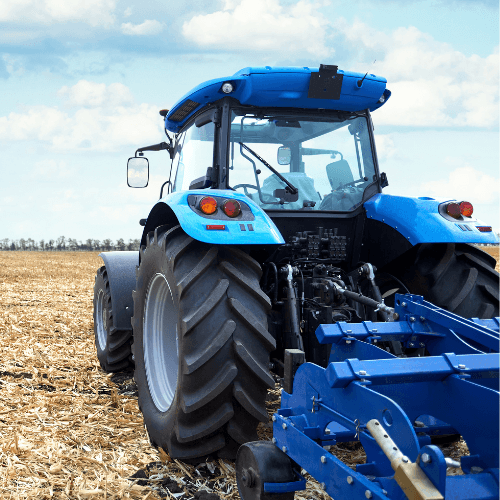 Tracteur bleu vu de l’arrière dans un champ moissonné, attelé à un outil de travail du sol