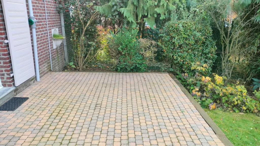 Terrasse pavée plane et dégagée le long d’un mur de briques, au pied d’une descente de gouttière