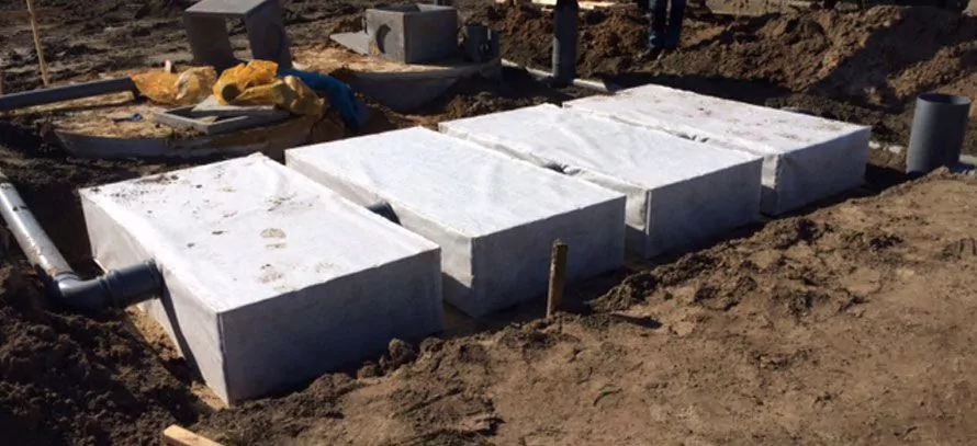 Quatre unités d’infiltration rectangulaires enveloppées d’un tissu blanc, posées côte à côte dans une tranchée et raccordées par des tuyaux
