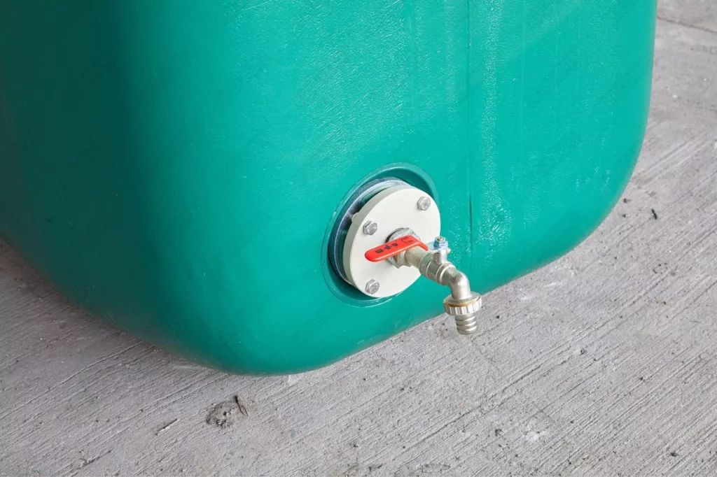Robinet à poignée rouge monté sur une bride blanche au bas d’une citerne verte