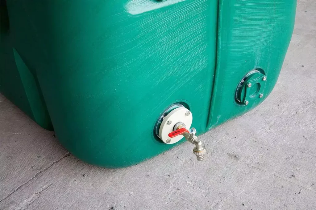 Robinet à poignée rouge monté sur une bride blanche au bas d’une citerne à eau de pluie verte