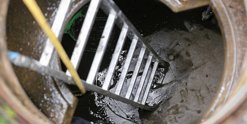 Échelle en aluminium descendant dans une citerne vide au fond couvert de boue